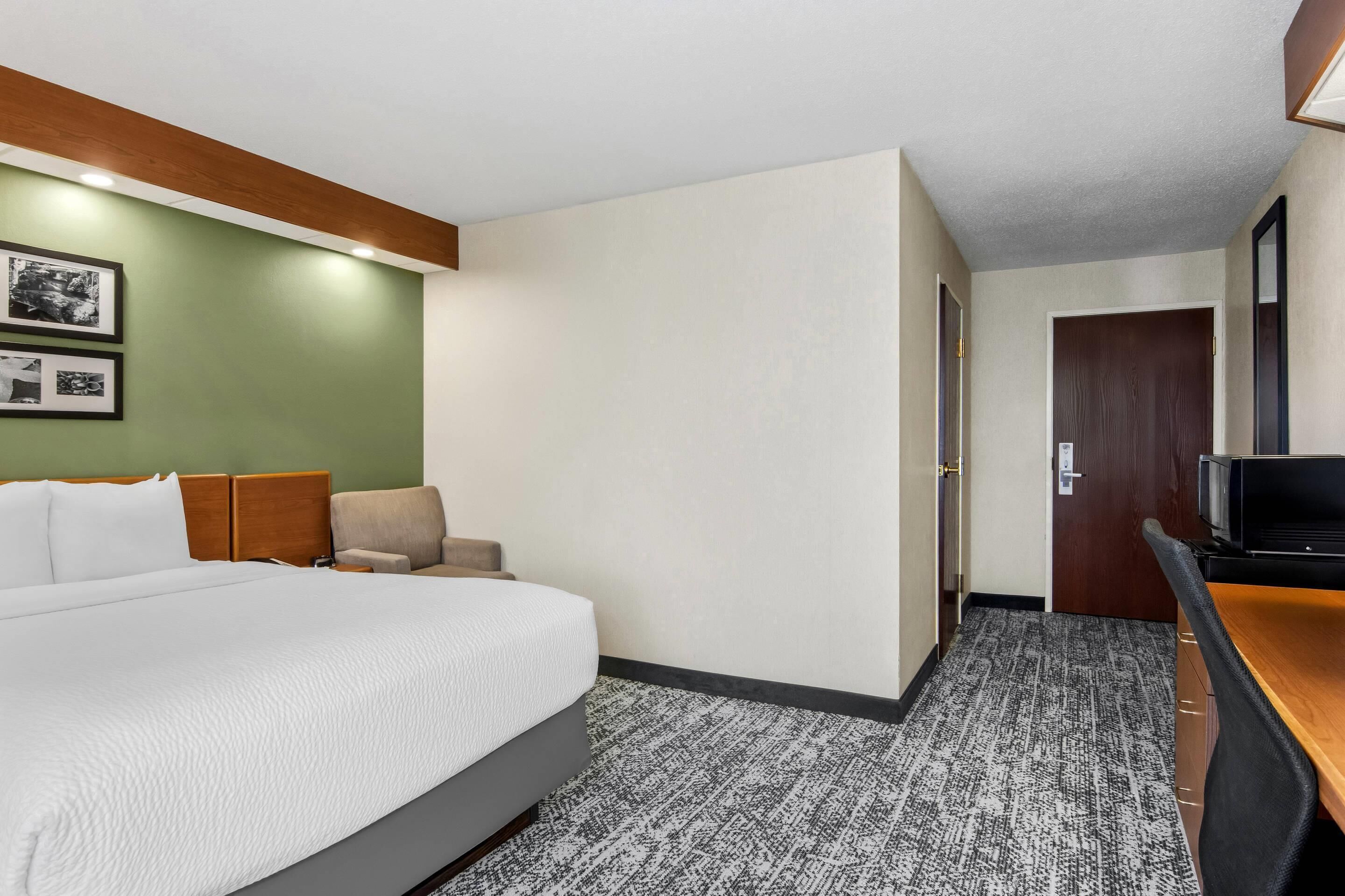 A hotel room with a bed, a desk, a television, and a door.