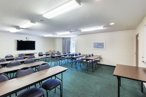 Uma sala de conferências com várias mesas e cadeiras, uma TV de tela plana e uma grande janela com cortinas.