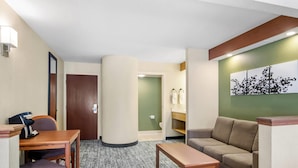 Habitació d'hotel amb escriptori de fusta, un sofà, una taula de café, una columna gran, una porta i una obra d'art penjada a la paret.