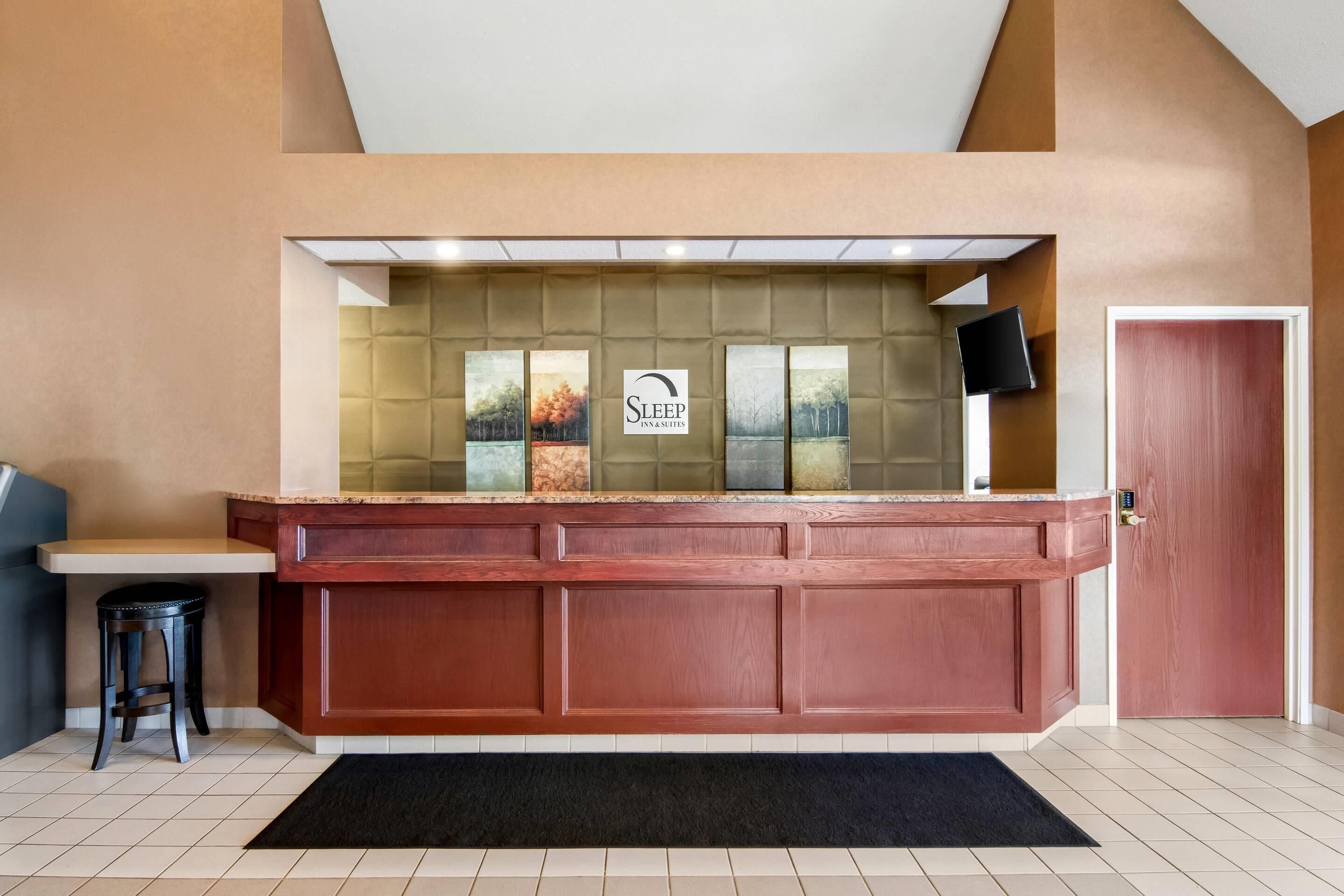 A reception area with a wooden counter, a black stool, a door, and a wall-mounted TV.