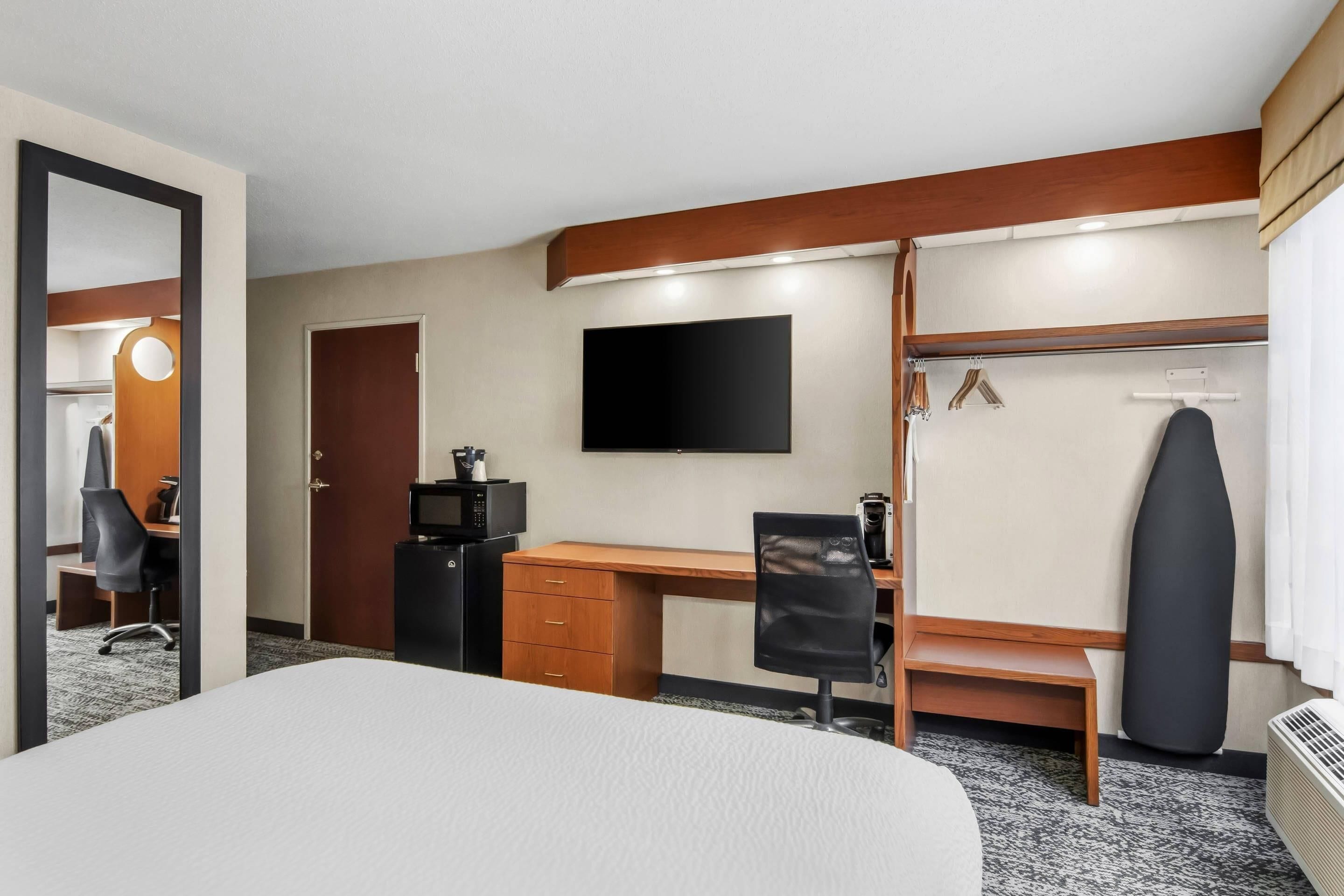 A hotel room with a bed, desk, chair, wardrobe, and a flat-screen TV.