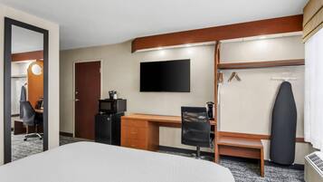 Habitación de hotel con cama, escritorio, silla, armario y televisor de pantalla plana.
