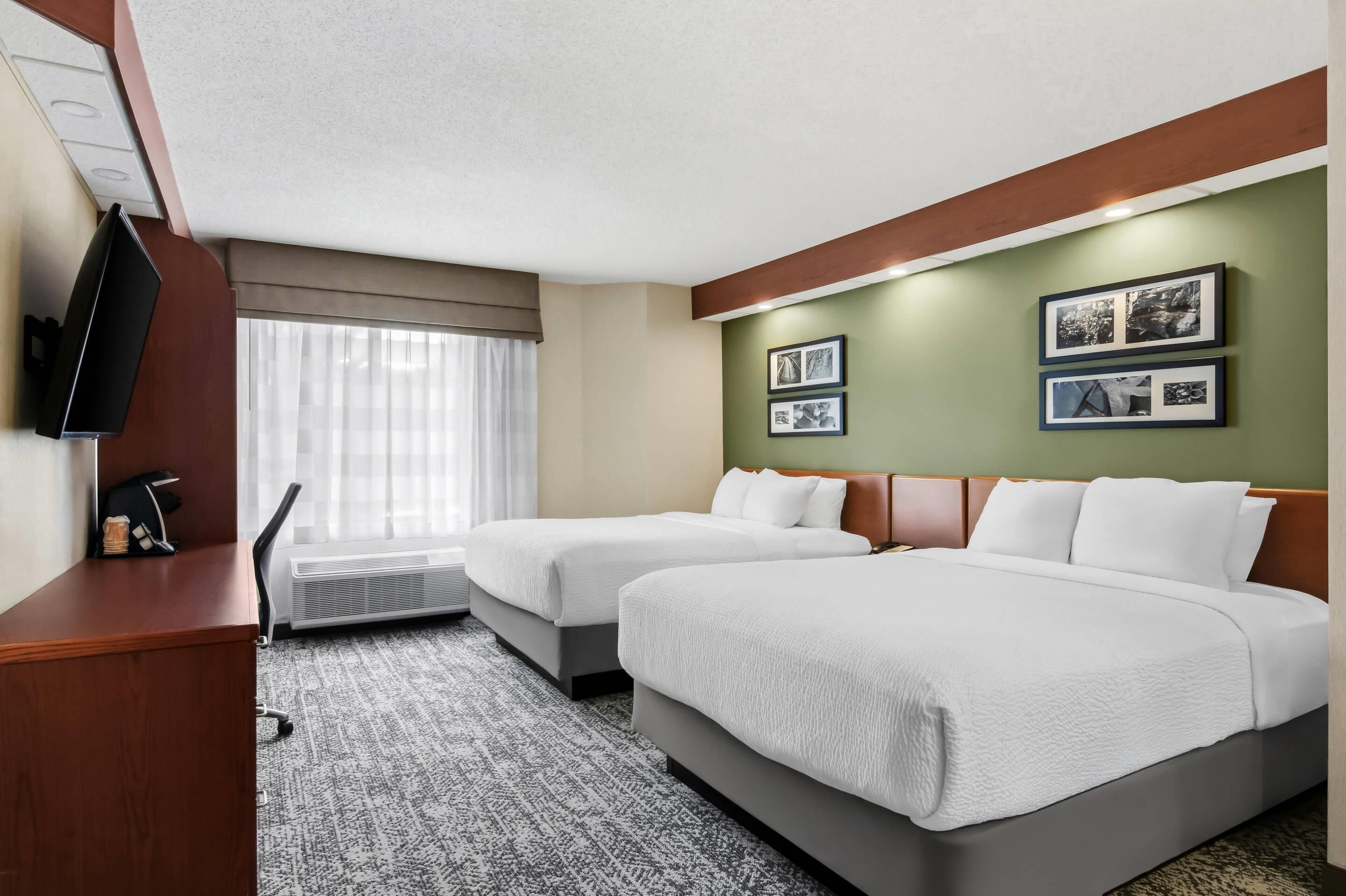 A hotel room with two beds, a desk, a TV, and a window with curtains.