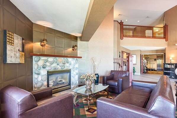 A spacious living area with leather sofas, a glass coffee table, a stone fireplace, and a staircase leading to an upper level. - Sleep Inn & Suites Bay View Acme - Traverse City (Williamsburg)