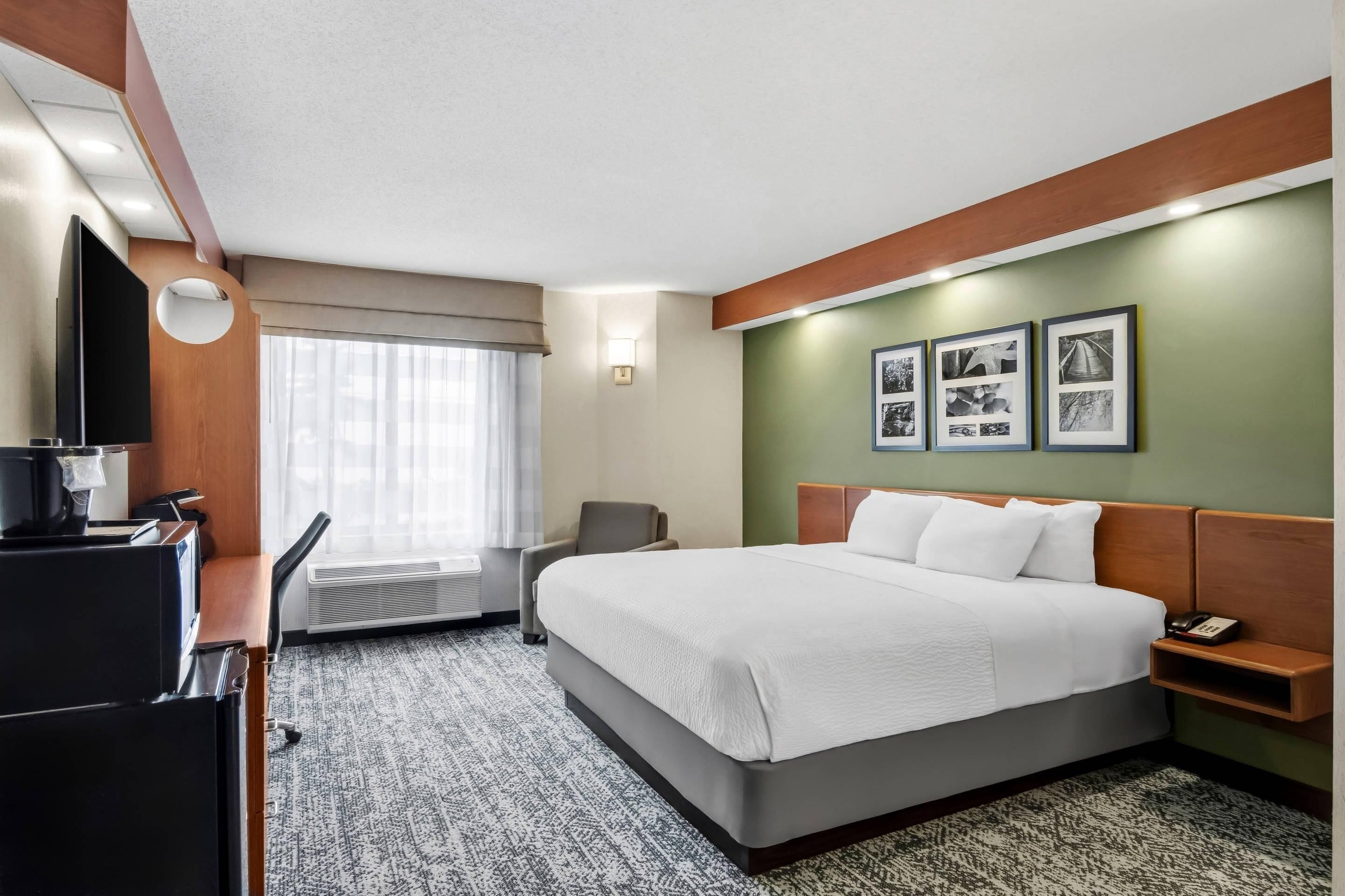 A hotel room with a bed, a desk with a computer, a chair, a TV, and a window with curtains.