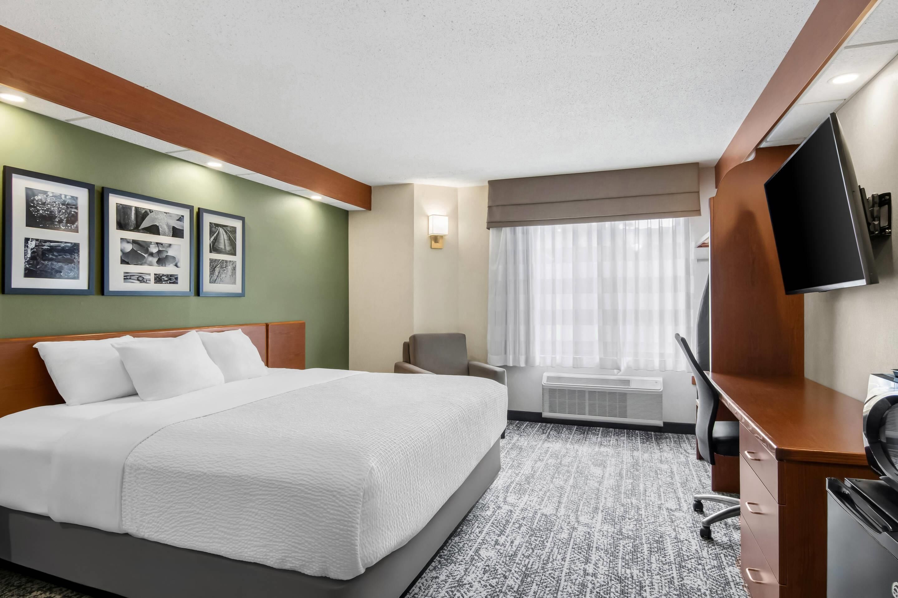 A hotel room with a bed, a desk, a chair, a TV, and framed pictures on the wall.