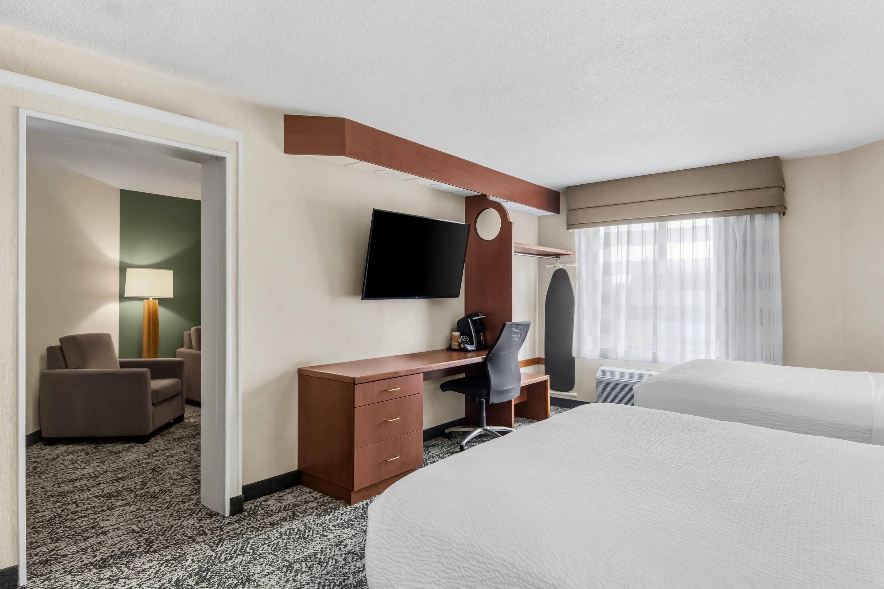 A hotel room with a bed, a desk with a chair, a TV, and a window with curtains.