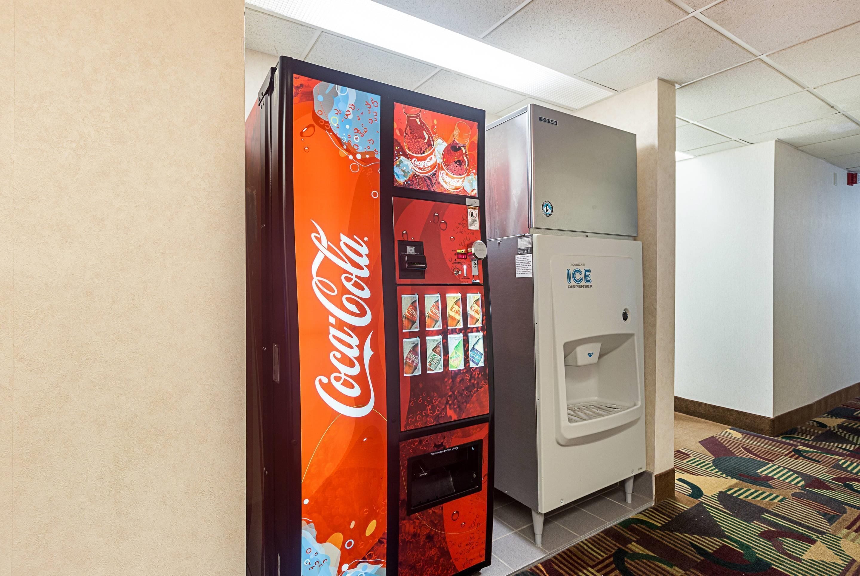 A vending machine with a Coca-Cola logo, a refrigerator, and a water dispenser in a hallway.