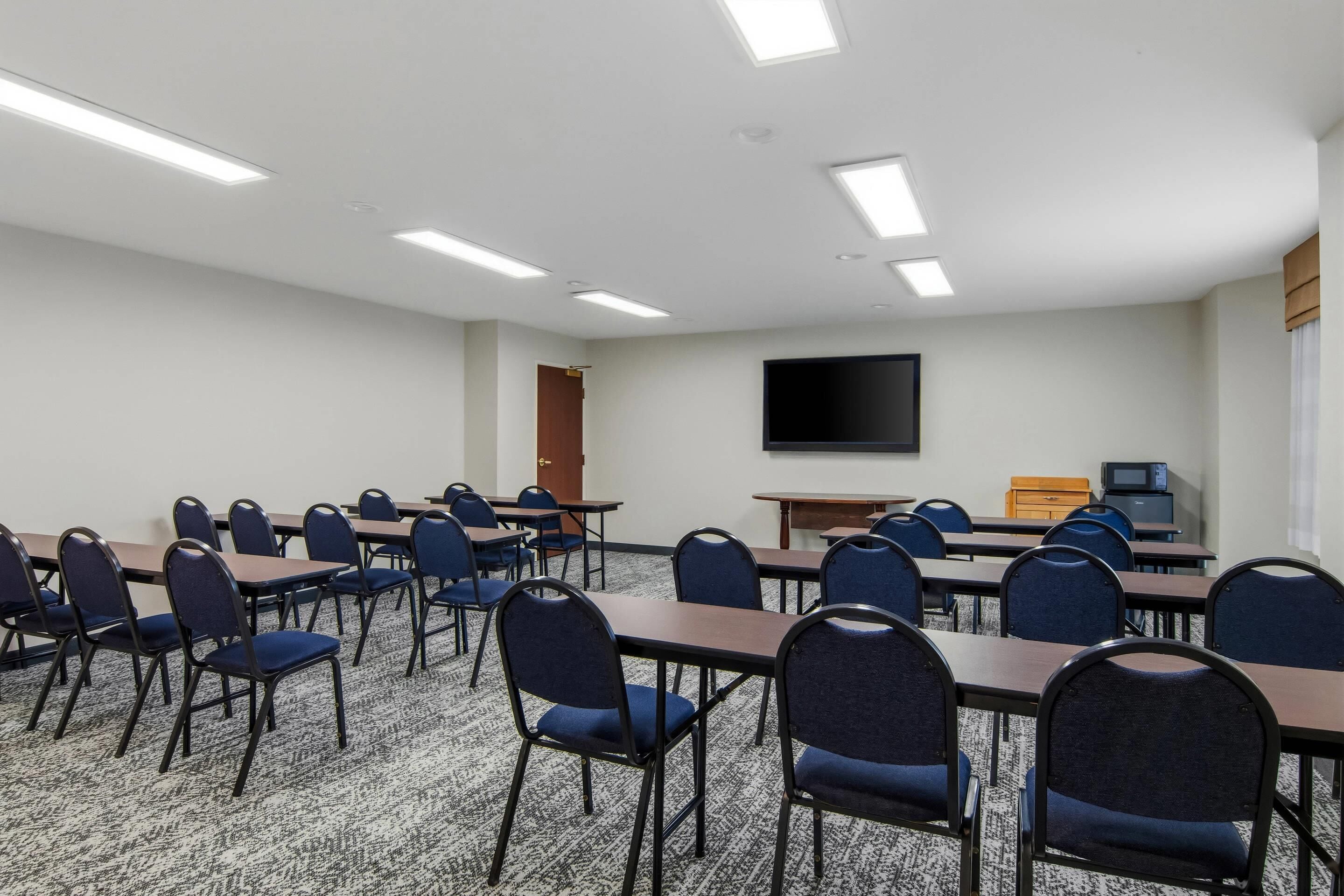 Une salle de conférence équipée de tables et de chaises, d’un téléviseur à écran plat et d’une porte.