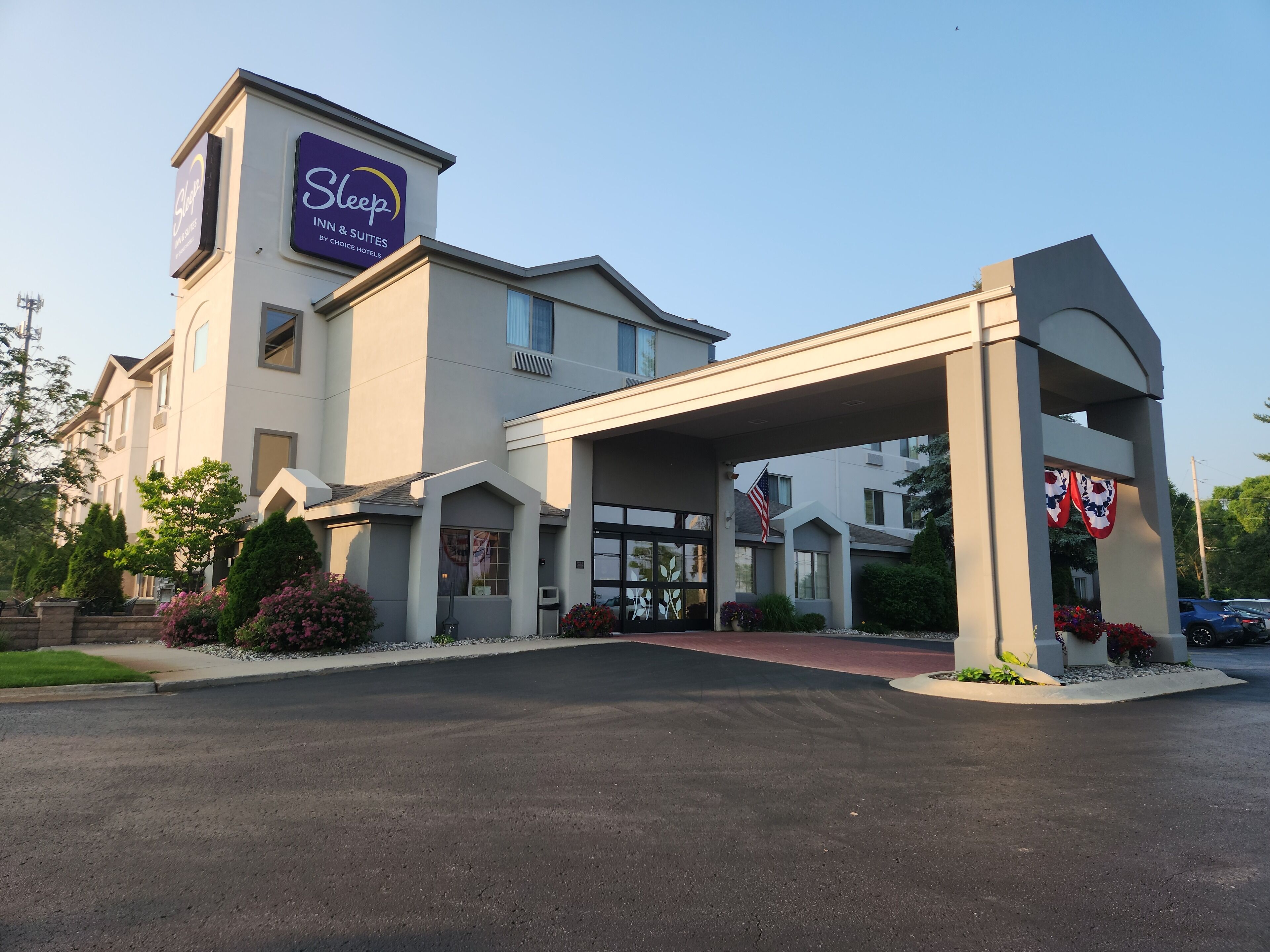 Un hotel con un llamativo letrero de Sleep Inn & Suites, una entrada techada y una bandera.