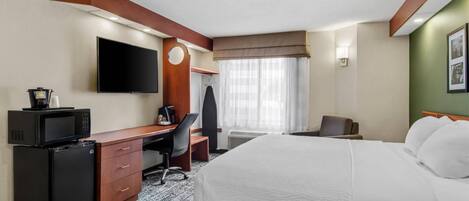 A hotel room with a bed, desk, microwave, refrigerator, TV, and a window with curtains.