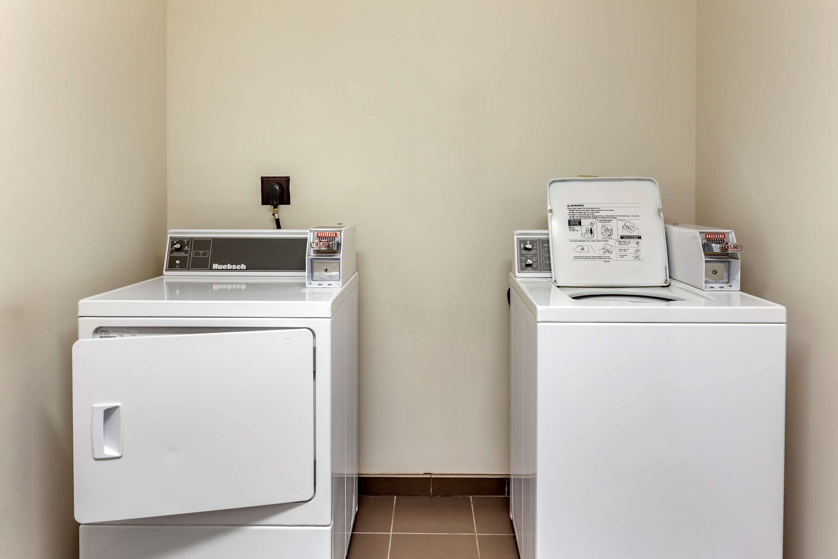 Un espace buanderie comprenant deux machines à laver à chargement frontal de couleur blanche et un sèche-linge, avec une prise de courant au mur.