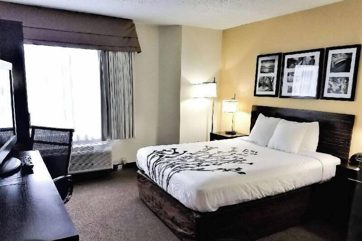 Quarto de hotel com cama, escrivaninha, abajur e três quadros na parede.