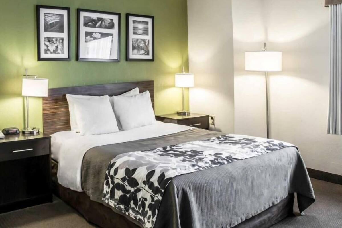 Quarto de hotel com uma cama, duas mesas de cabeceira, um criado-mudo, um abajur e três quadros na parede.