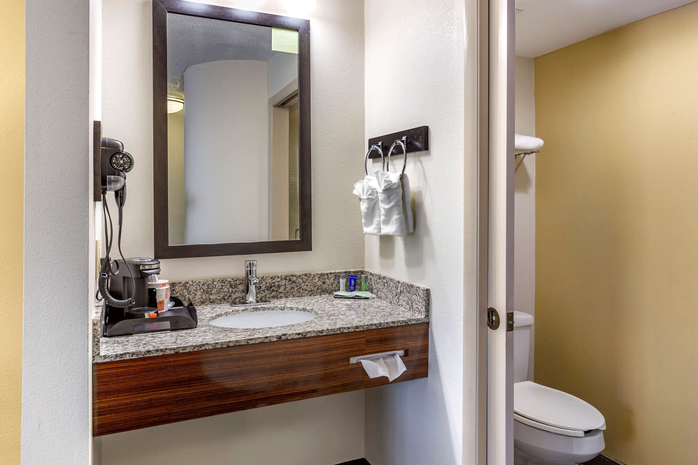A bathroom with a granite countertop sink, a mirror, a towel rack, and a toilet.