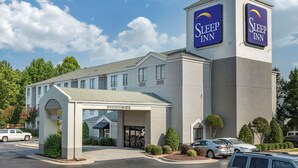 A Sleep Inn hotel with a clear entrance, a sign indicating a 12'-4" clearance, and a parking area with several cars.
