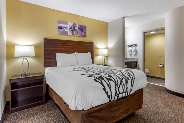 A hotel room with a large bed, two bedside tables with lamps, a wooden headboard, and a wall-mounted artwork.