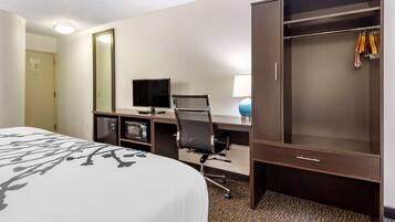 A hotel room with a bed, a desk with a computer, a chair, a wardrobe, and a mirror.