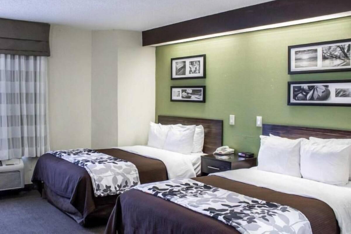 A hotel room with two beds, a nightstand, a telephone, and framed pictures on the wall.
