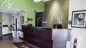 A modern hotel reception area with a green wall, a dark reception desk, and a framed artwork on the wall. - Sleep Inn Garner - Clayton (Garner)