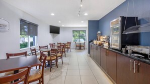 A restaurant with wooden tables and chairs, a kitchen area, and a sign on the wall. - Sleep Inn Garner - Clayton (Garner)