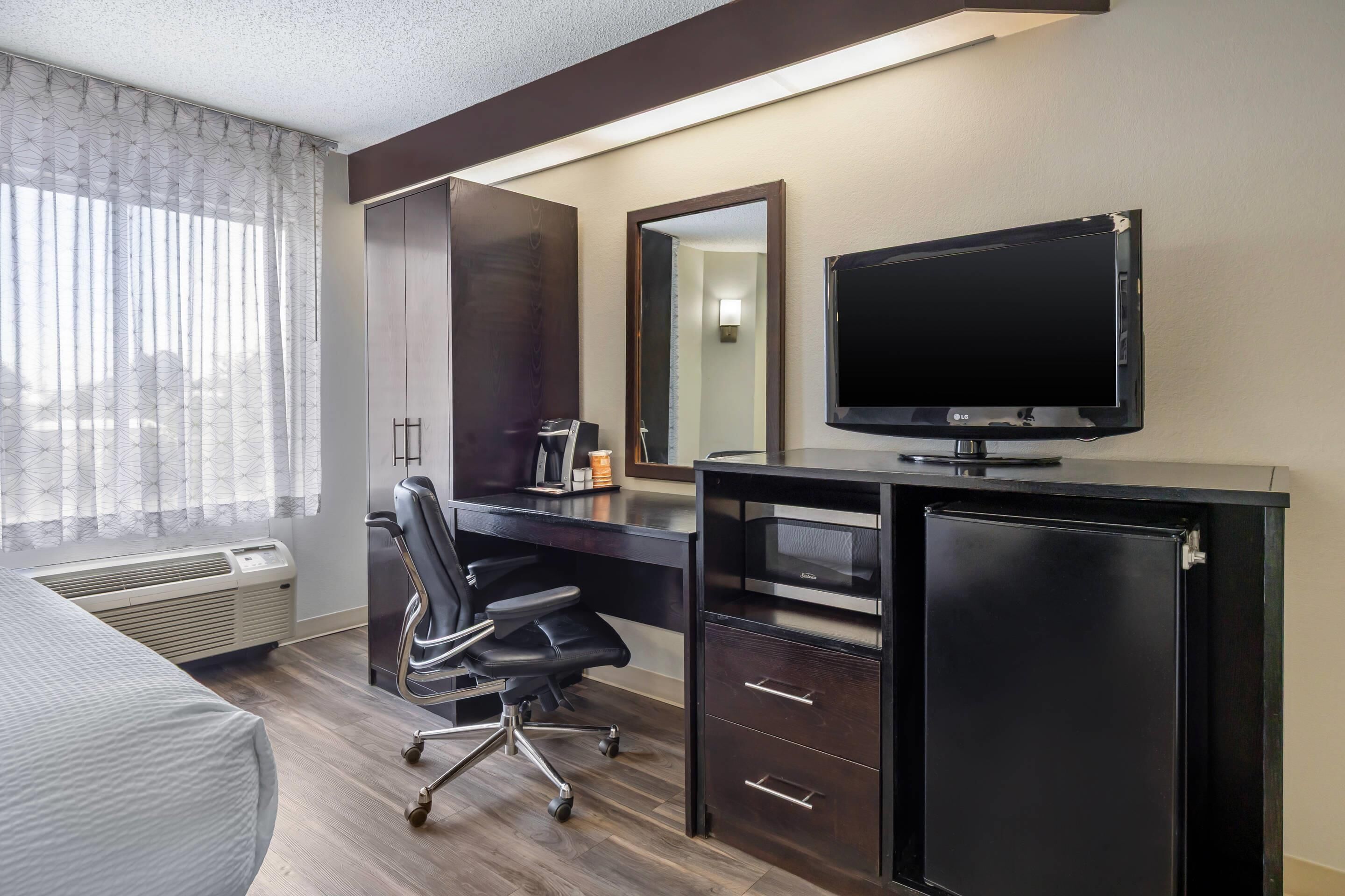 A hotel room with a bed, a desk with a chair, a television, a mirror, and a heater.