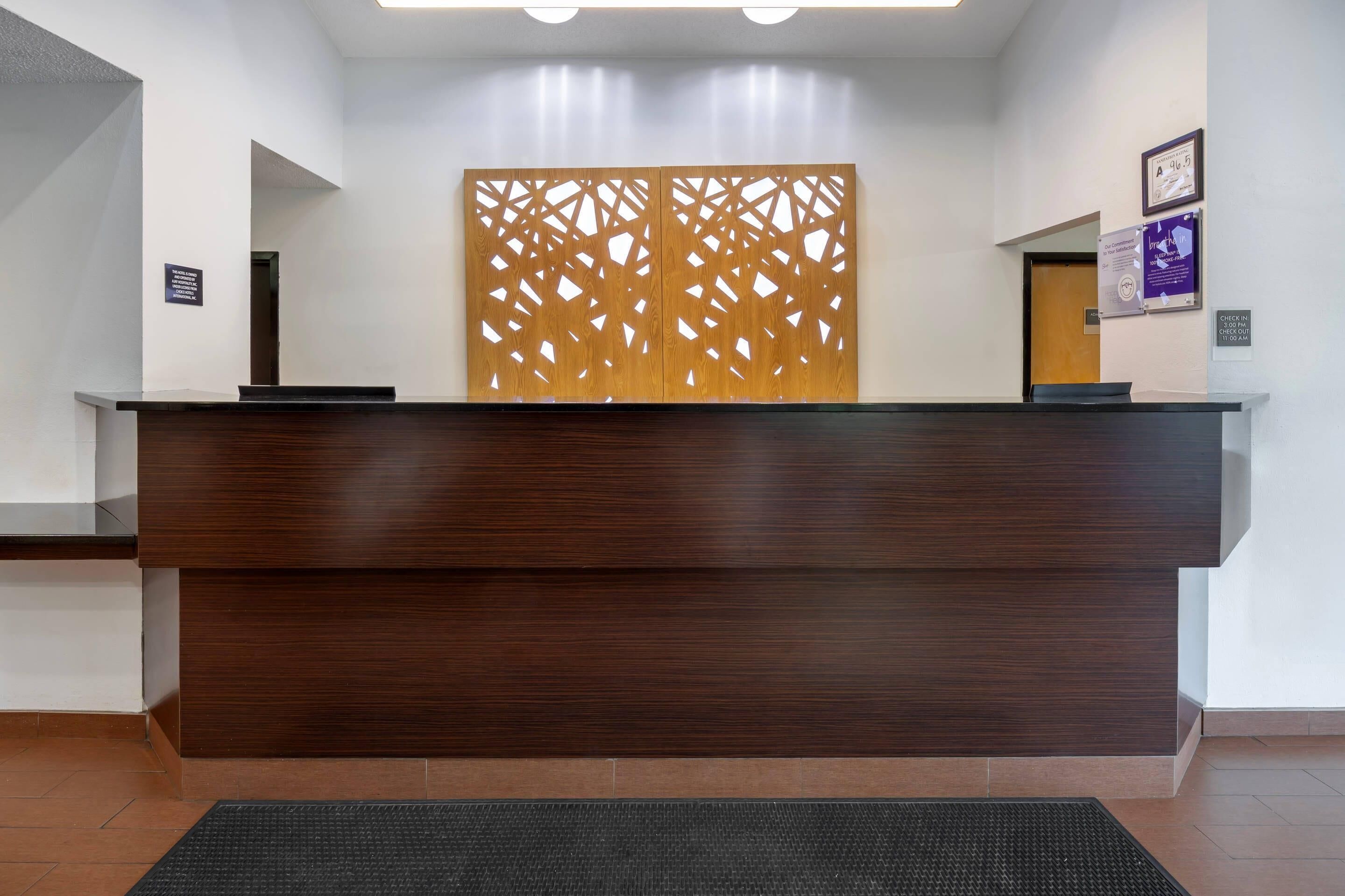 A reception desk with a wooden panel backdrop, a black mat at the entrance, and a door to the right.