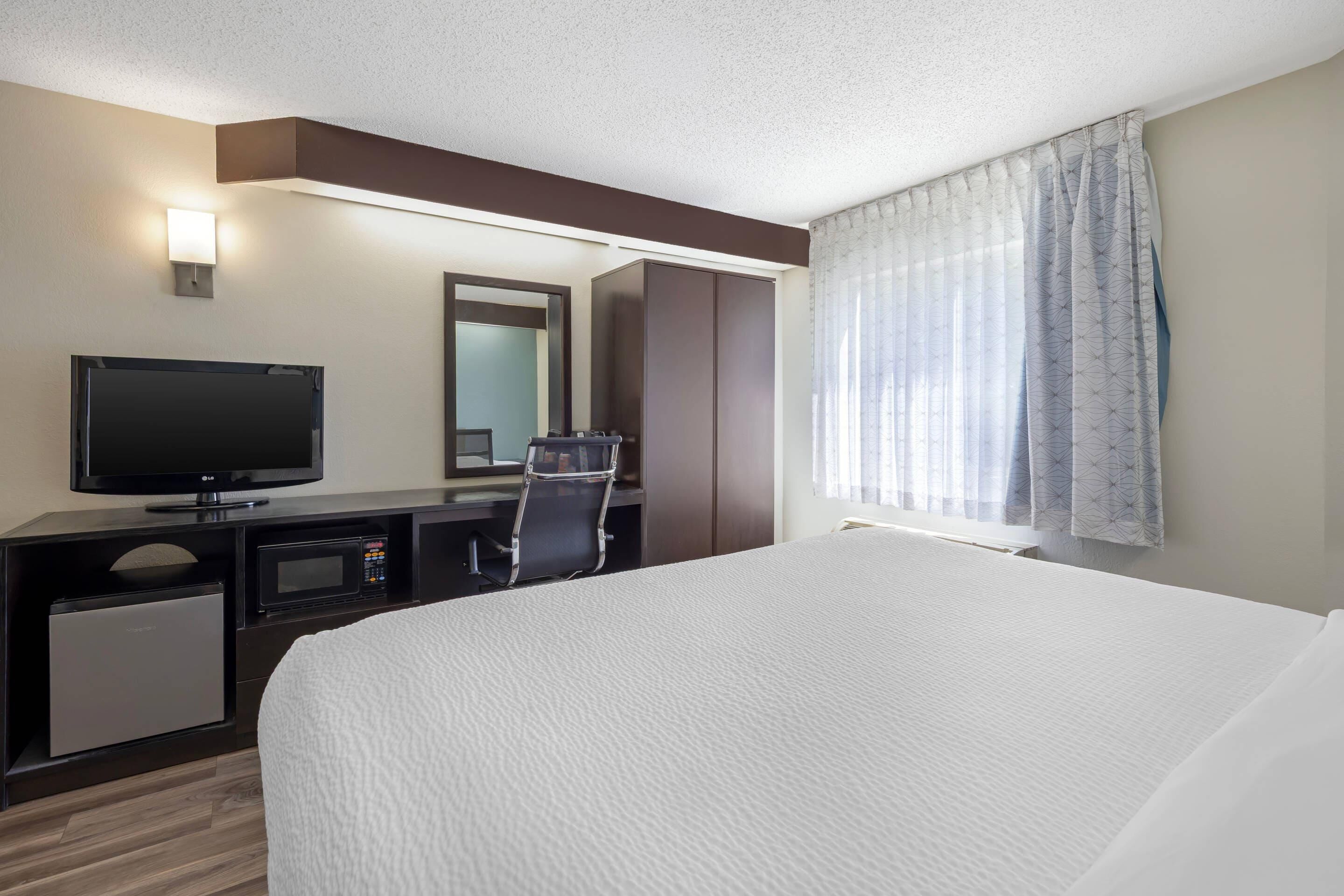A hotel room with a bed, a television, a desk with a chair, a microwave, and a small refrigerator.