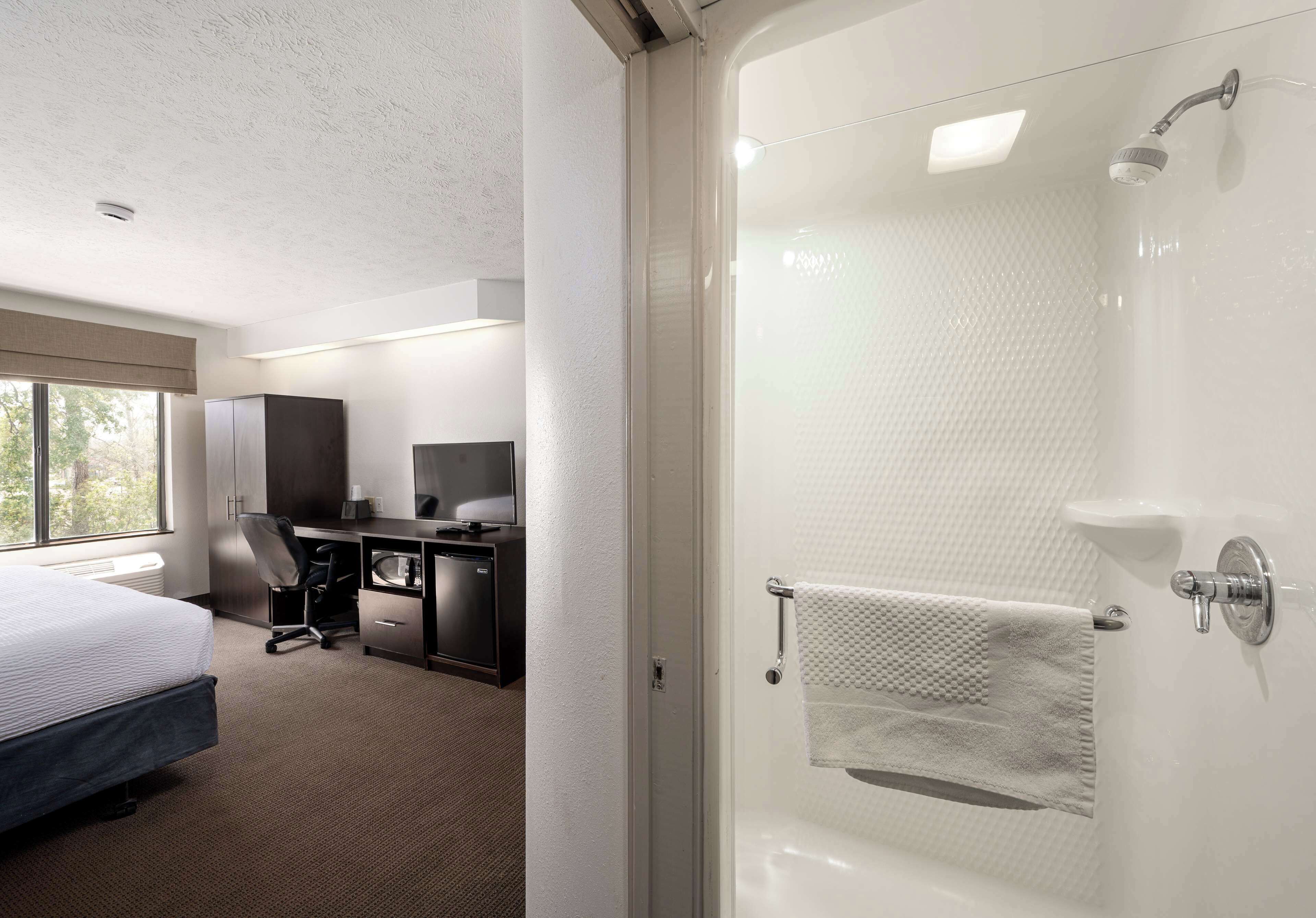 A hotel room with a bed, desk, chair, and a shower area.