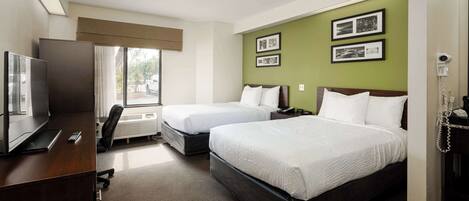 A hotel room with two beds, a desk with a computer, a chair, and a window with a view of the outside.