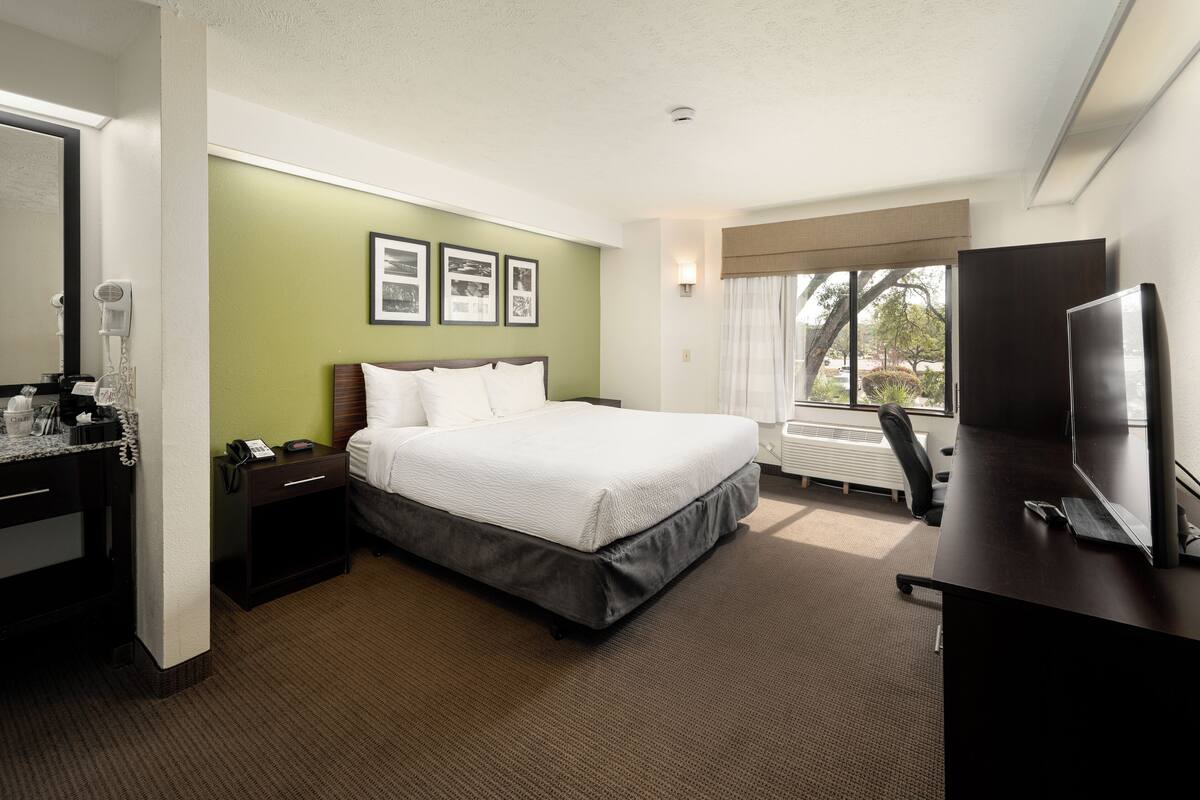 A hotel room with a bed, a desk, a chair, a TV, and a window with a view.