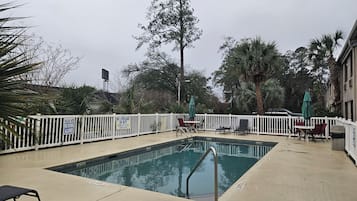 Una piscina con valla blanca, sillas de descanso y sombrillas.