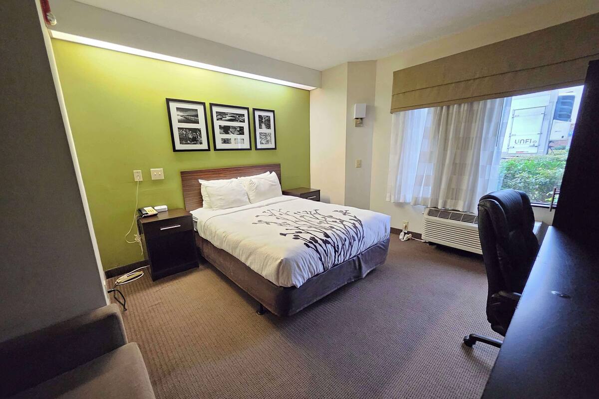 A hotel room with a bed, bedside tables, a desk, a chair, a window with curtains, and three framed pictures on the wall.