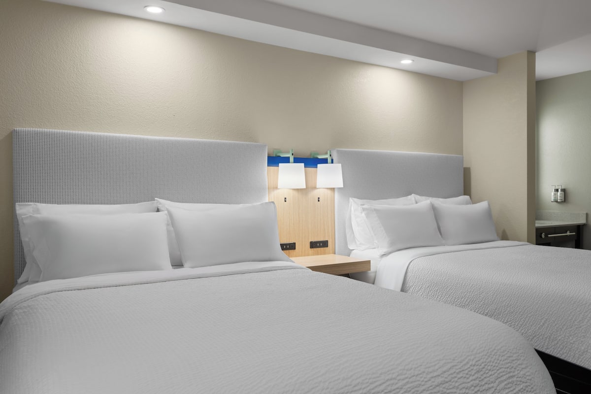 A hotel room with two beds, a wooden wardrobe, and a nightstand with a lamp.