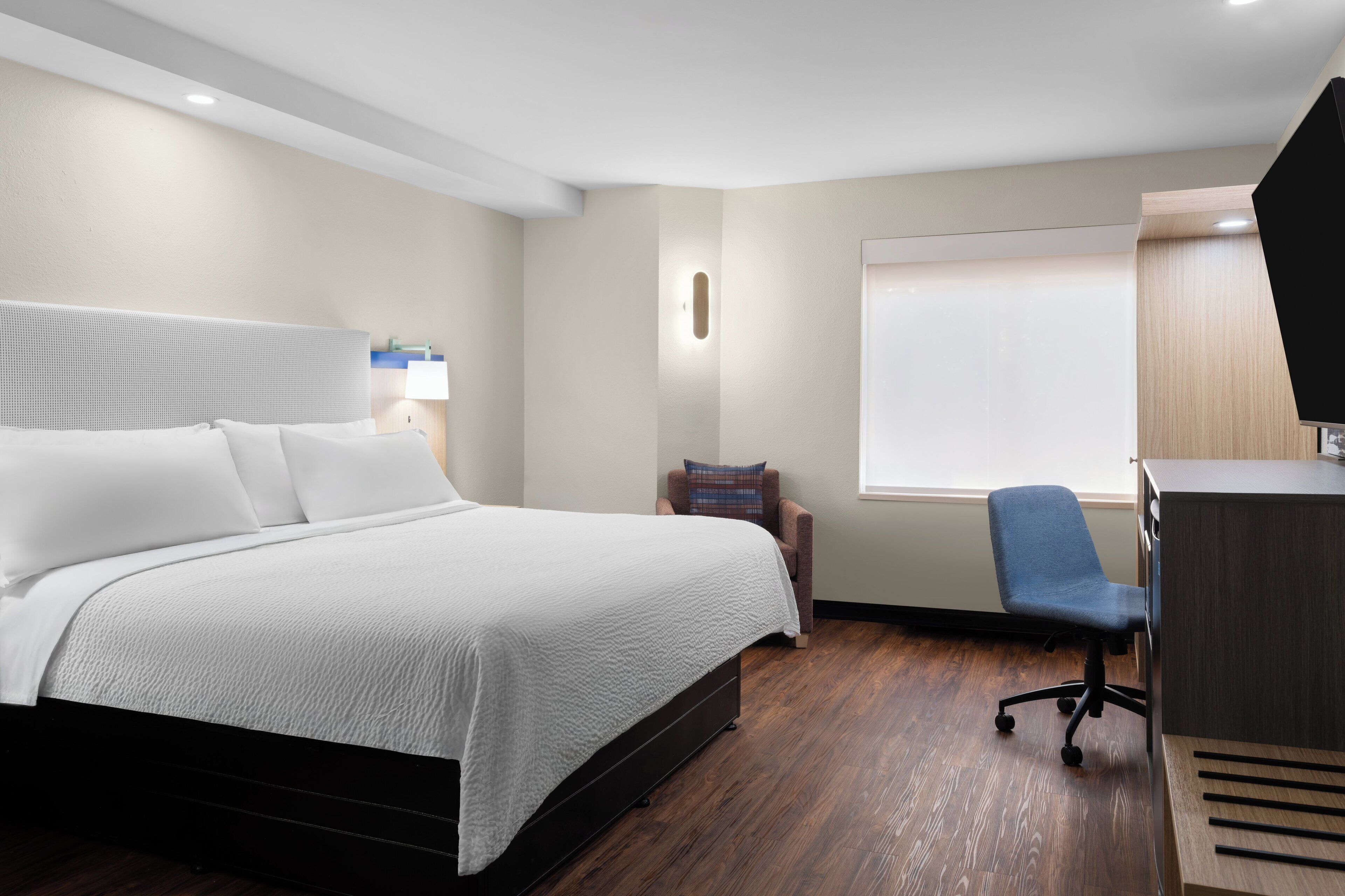 Una habitación de hotel con cama, escritorio, silla y ventana.