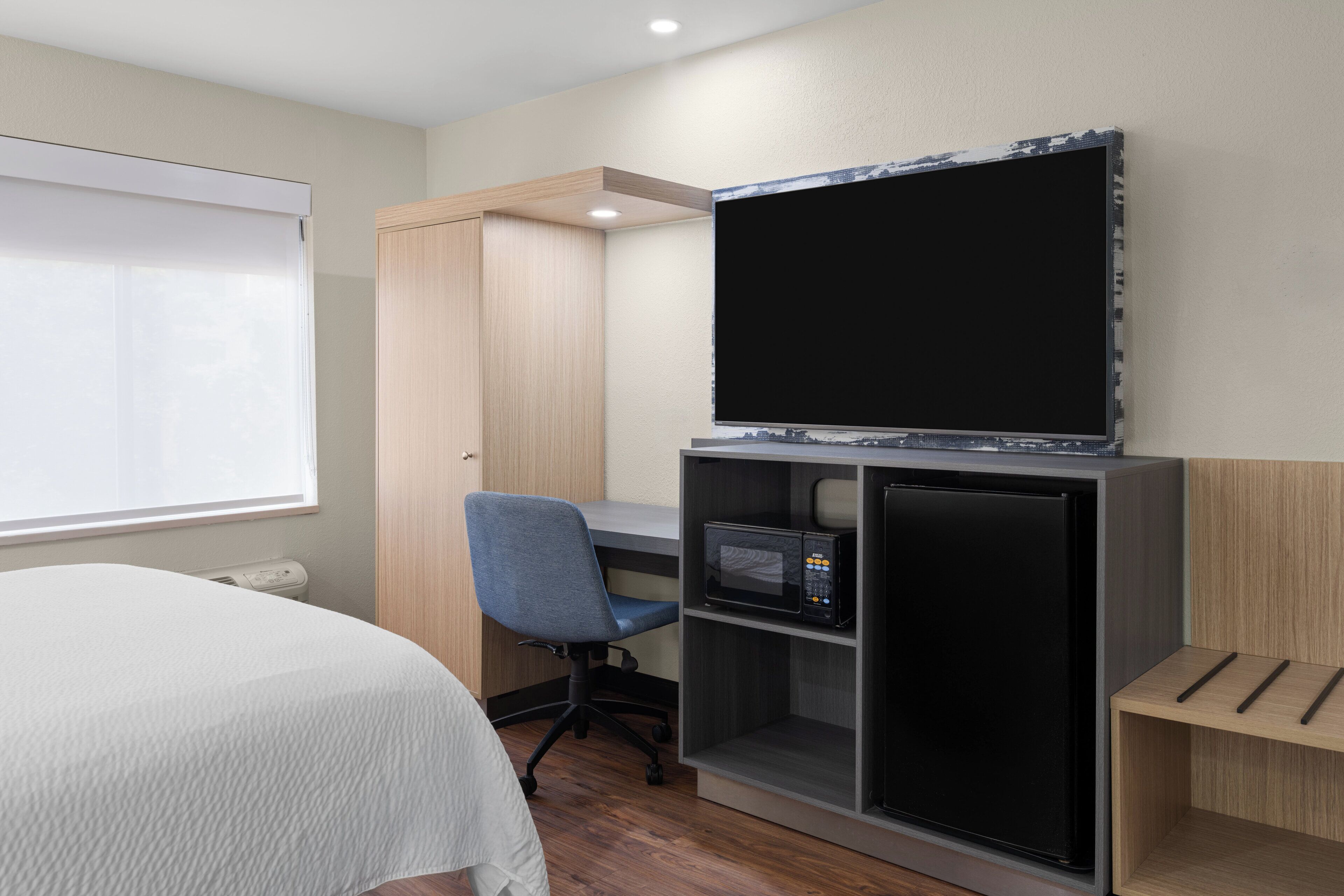 Ett hotellrum med en säng, ett skrivbord med en dator, en tv och en mikrovågsugn.