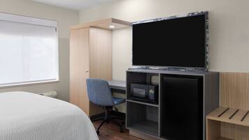 A hotel room with a bed, a desk with a computer, a TV, and a microwave.