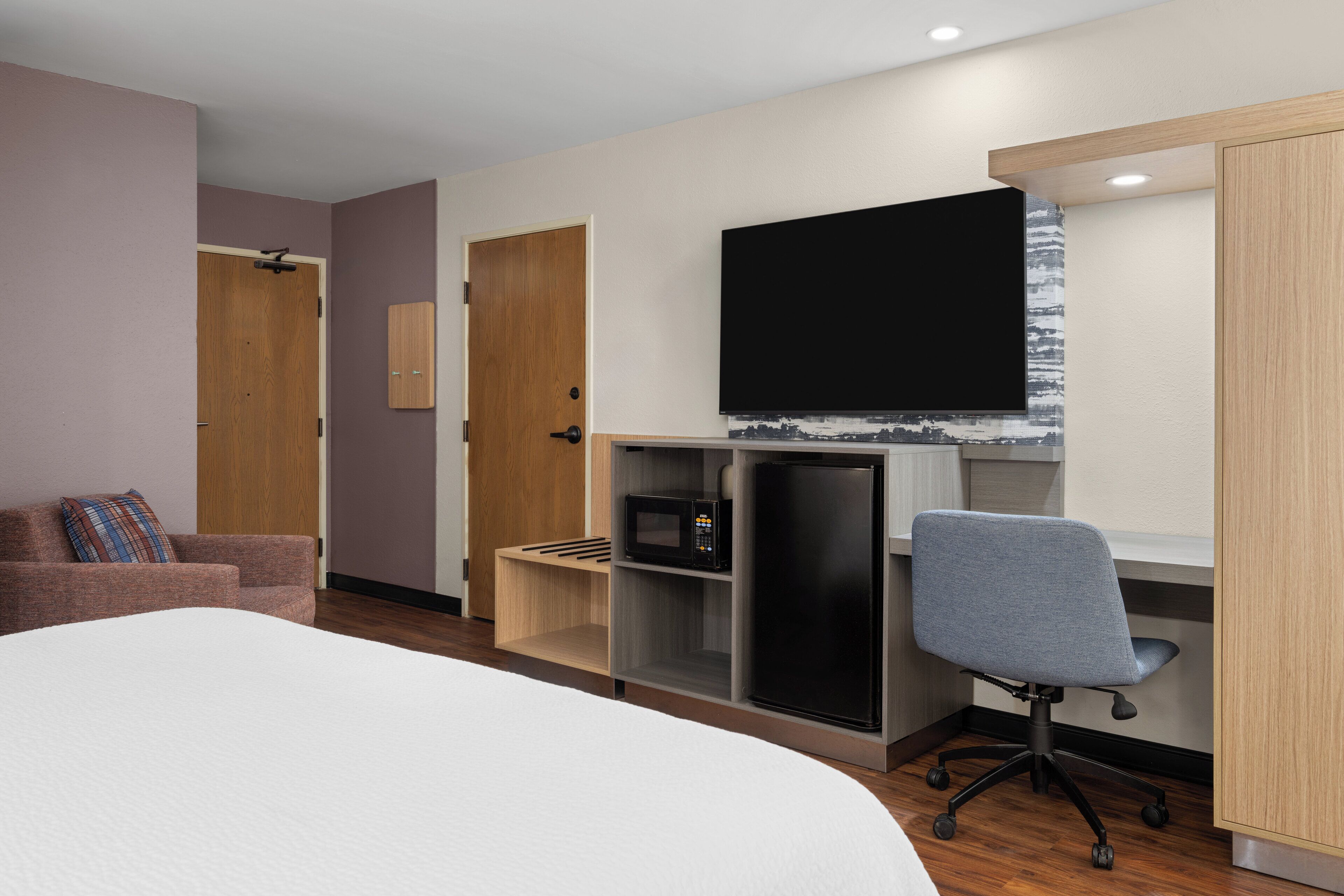 Une chambre d’hôtel équipée d’un lit, d’un bureau avec un ordinateur, d’une chaise, d’une télévision et d’une armoire.