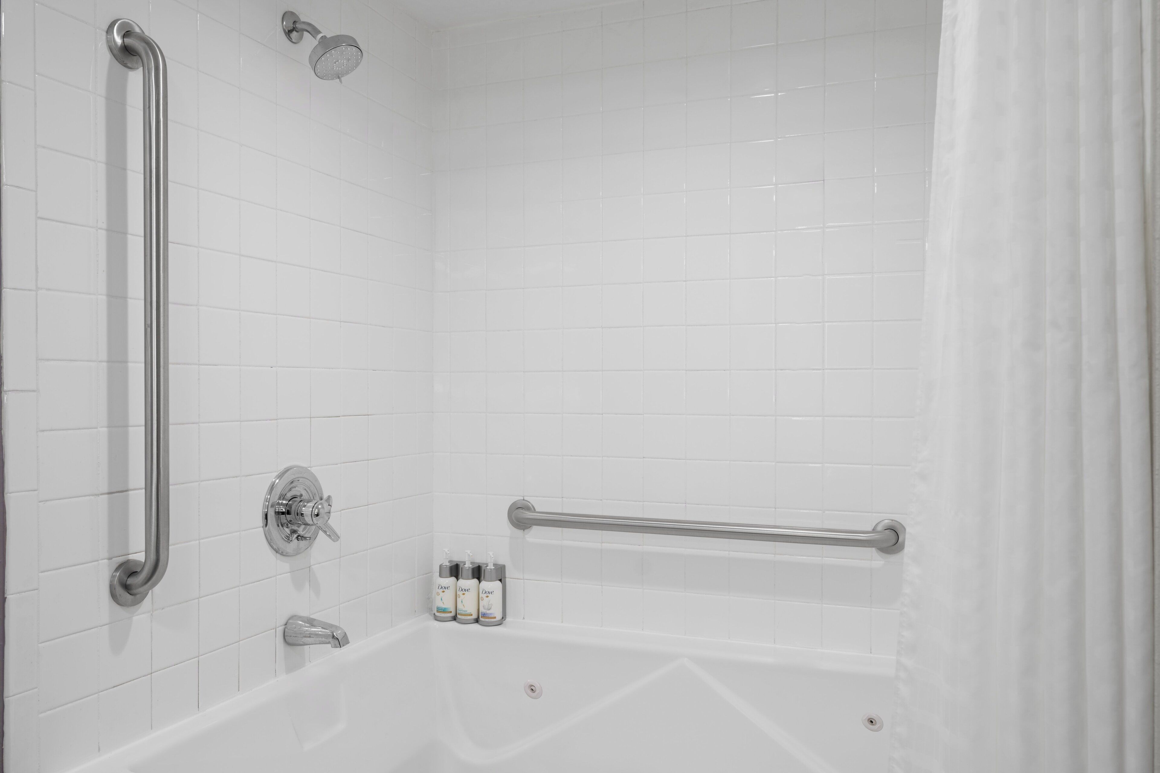 A white tiled shower with a handheld showerhead, a handheld shower control, and a handheld shower head mounted on the wall.