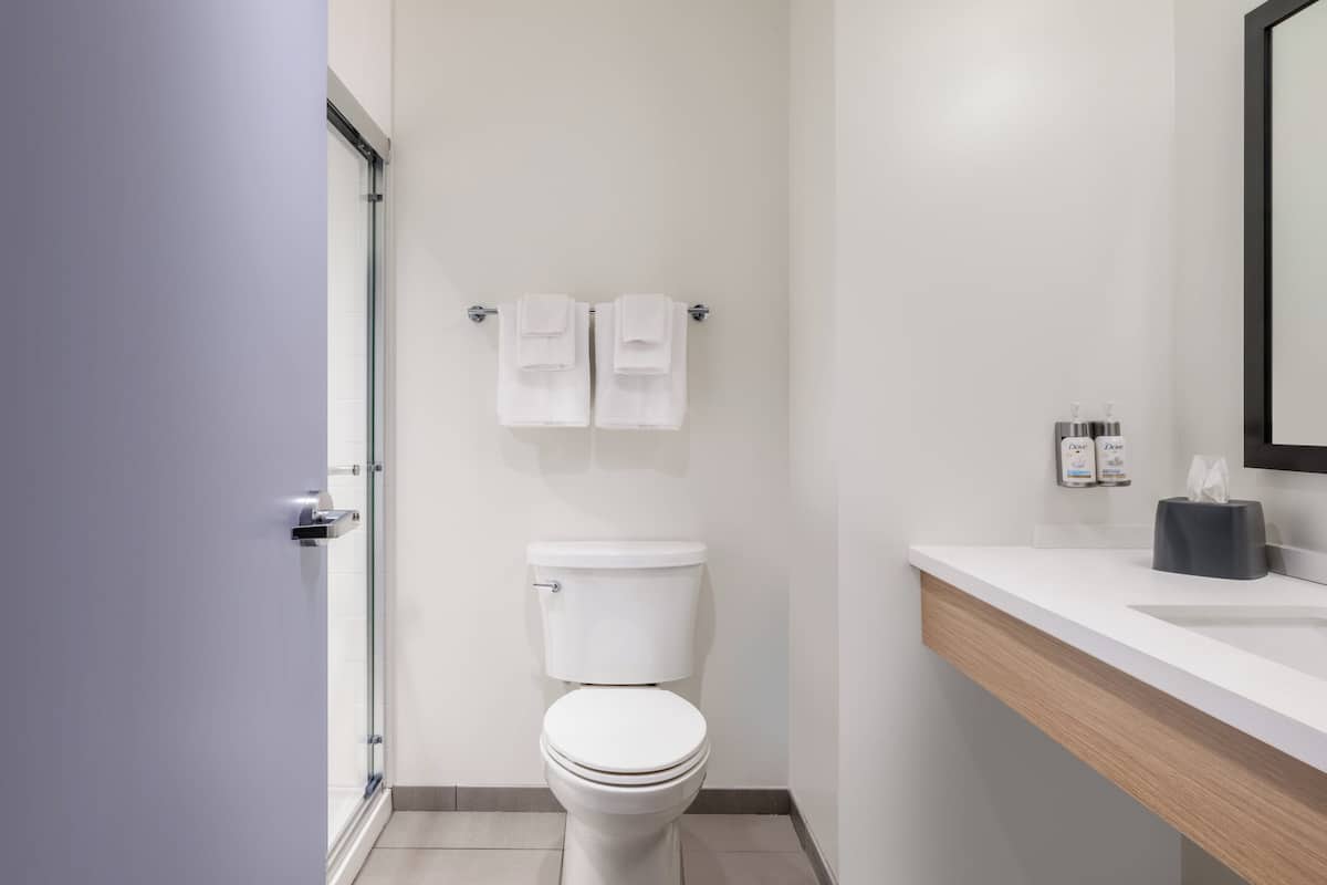 A modern bathroom with a white toilet, a glass shower enclosure, a wooden vanity with a mirror, and two towels hanging on a rack.