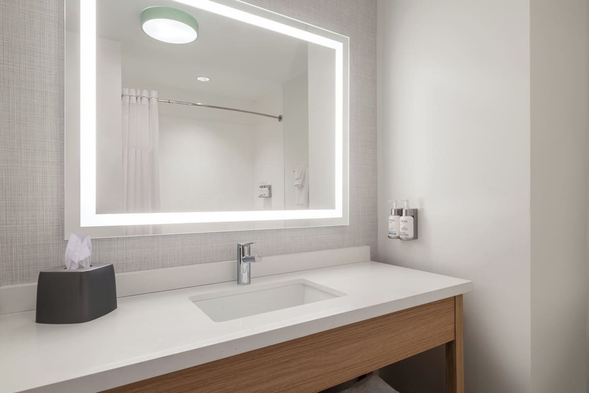 A modern bathroom with a large mirror, white sink, and wooden vanity.