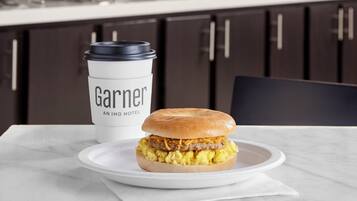 A breakfast setting with a sandwich on a plate, a coffee cup, and a menu board in the background.