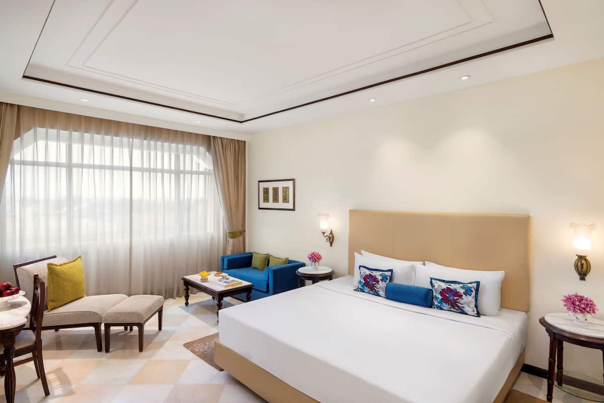 A hotel room with a large bed, a sofa, a dining table, and a small side table.