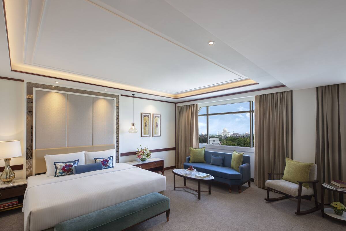 A hotel room with a large bed, a sofa, a rocking chair, a coffee table, and a view of the city through the window.