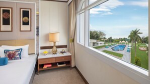 A hotel room with a bed, bedside table, lamp, framed artwork, and a view of a swimming pool and garden. - Tajview,Agra-IHCL SeleQtions (Agra)