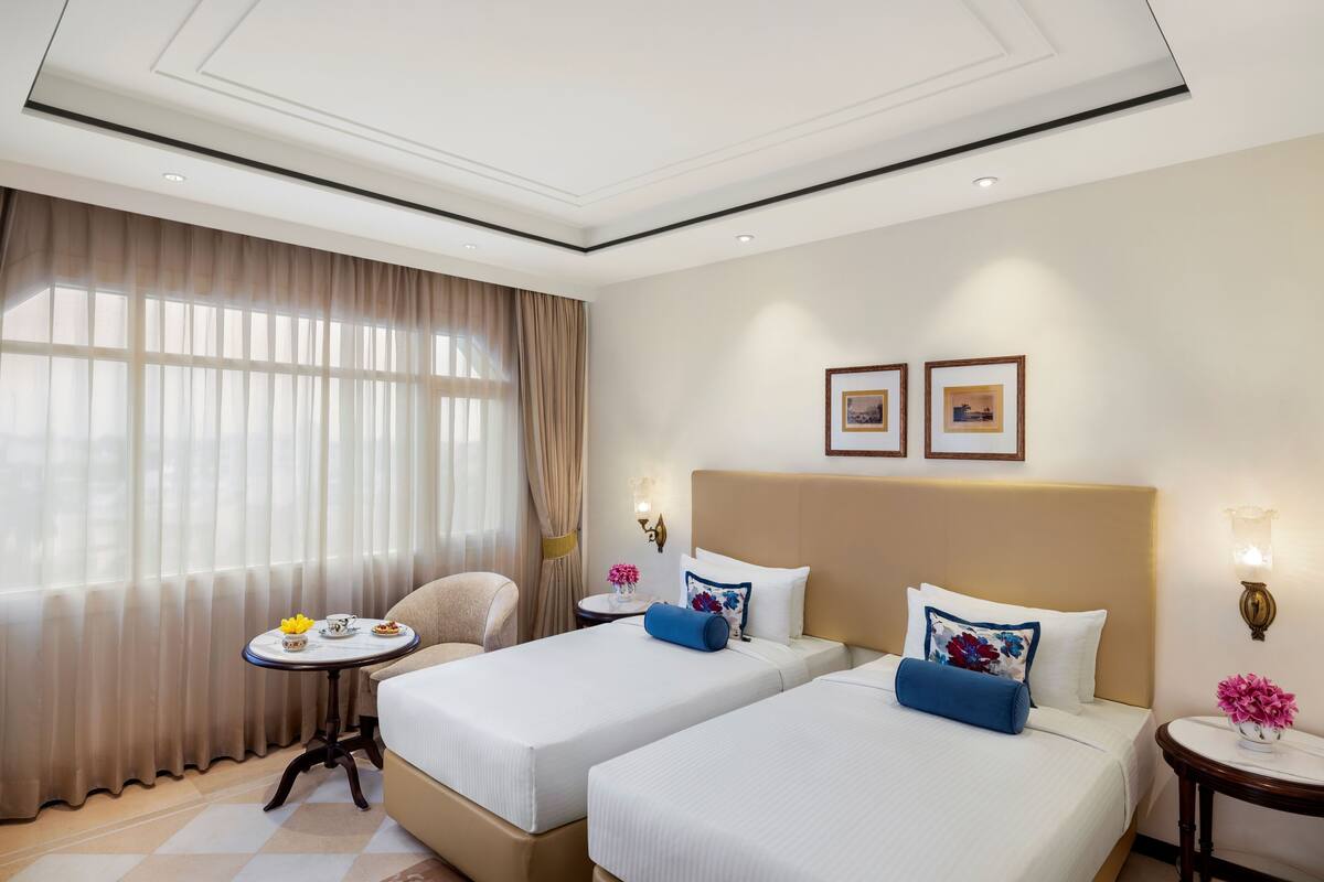 A hotel room with two beds, a small table with a vase of flowers, and a chair.