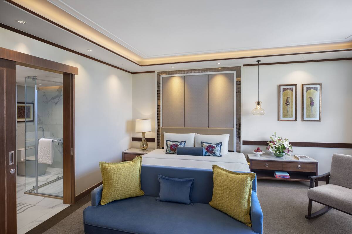 A hotel room with a bed, a sofa, a nightstand, a lamp, and a shower area.