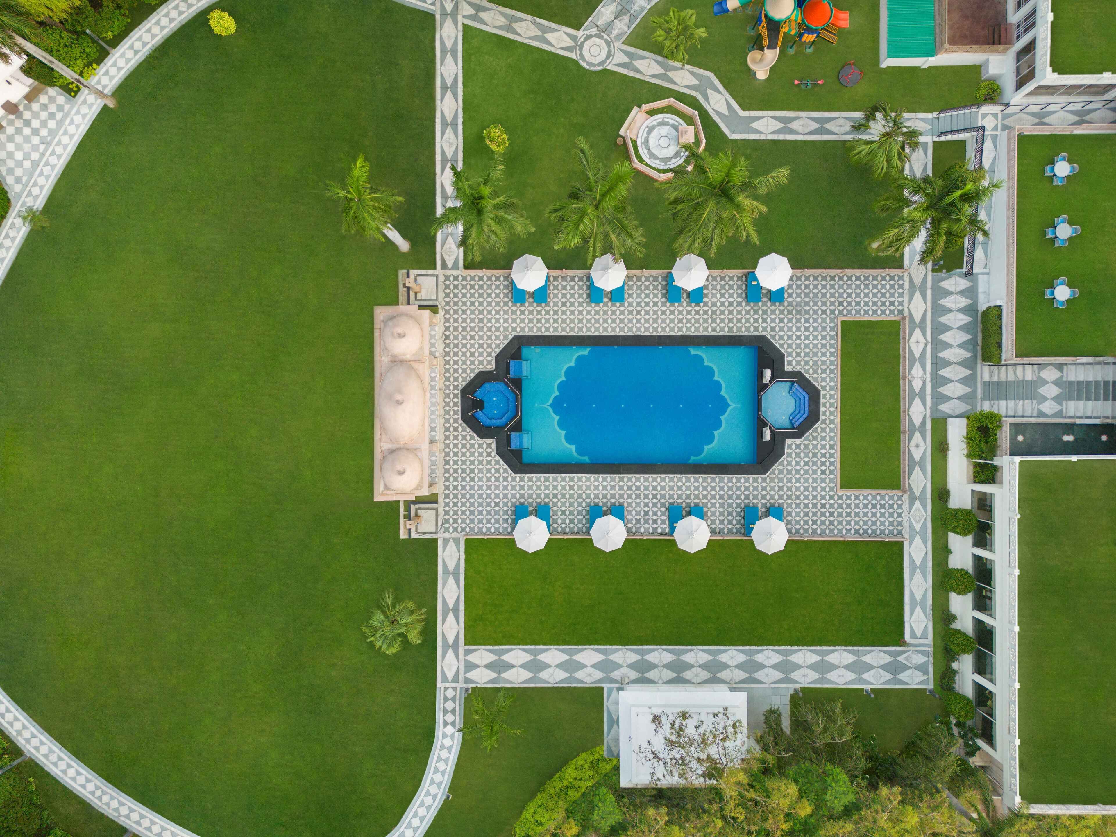Vista aérea de una zona de piscina con una pileta rectangular, tumbonas y una pequeña fuente circular.