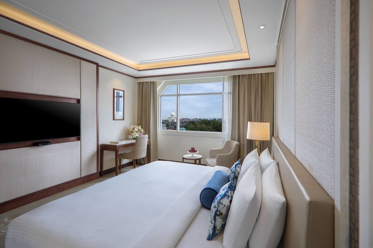 A hotel room with a large bed, a desk, a chair, a TV, and a window with a view.
