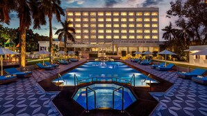A hotel with a large swimming pool, sun loungers, and palm trees. - Tajview,Agra-IHCL SeleQtions (Agra)